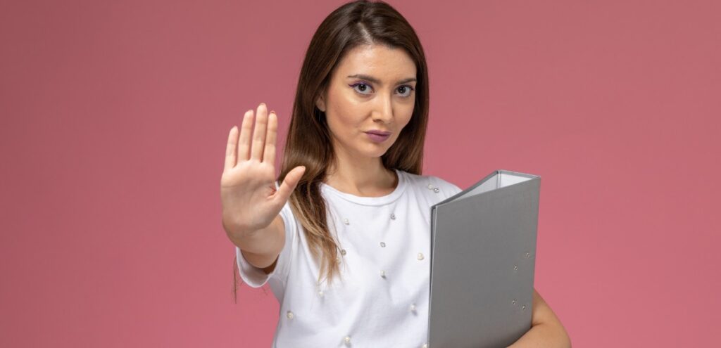Foto de uma mulher em um fundo rosa com uma mão para frente e a outra segurança uma pasta, simbolizando que está na hora de implementar o RH digital.
